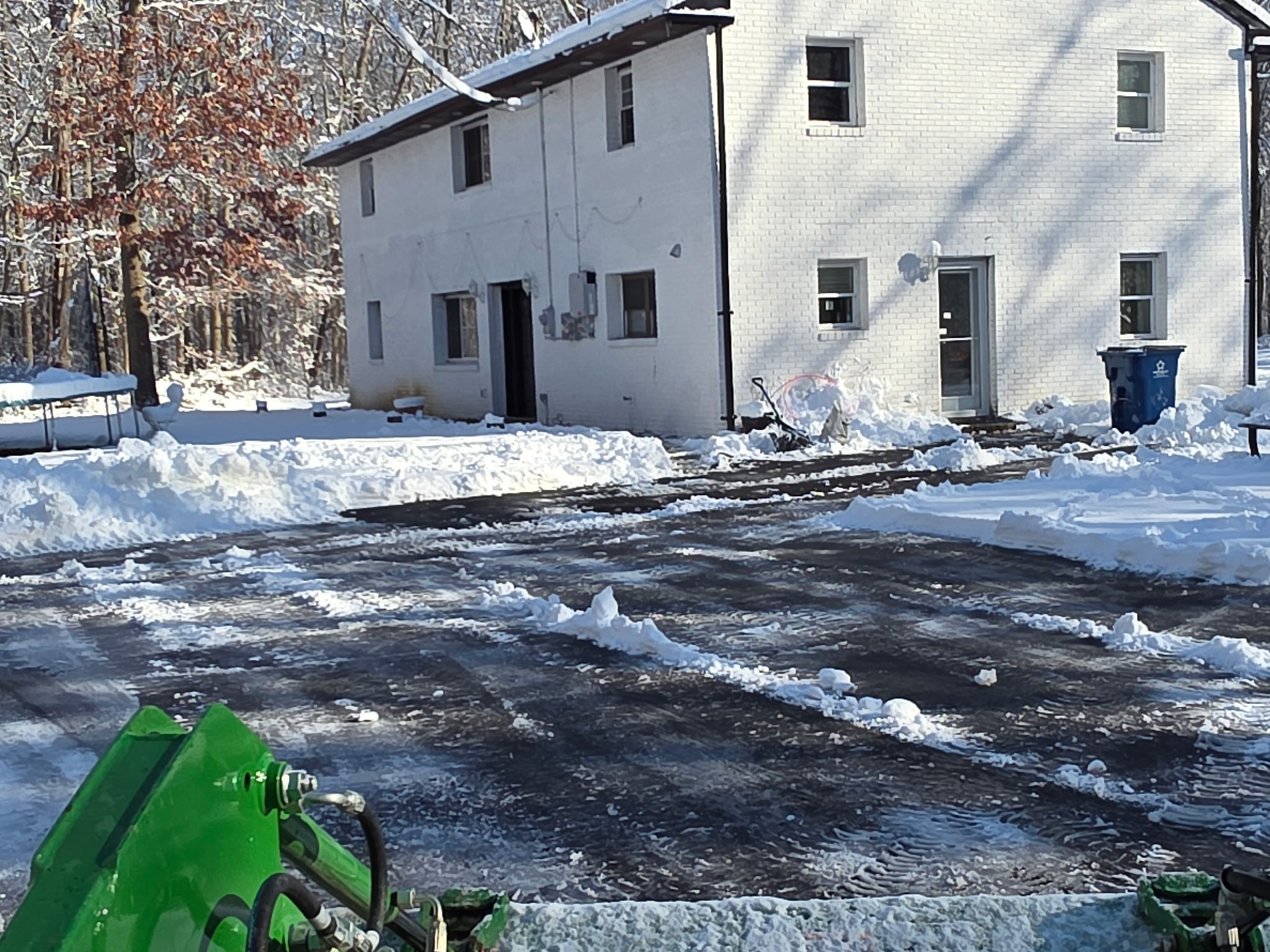 Snow-removal equipment clearing a residential driveway with snow piled along the edges